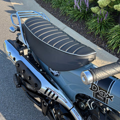 Mounted black tuck-and-roll Honda DAX 125 seat cover with pale blue piping, shown beside the chrome rack, handmade by Cheeky Seats